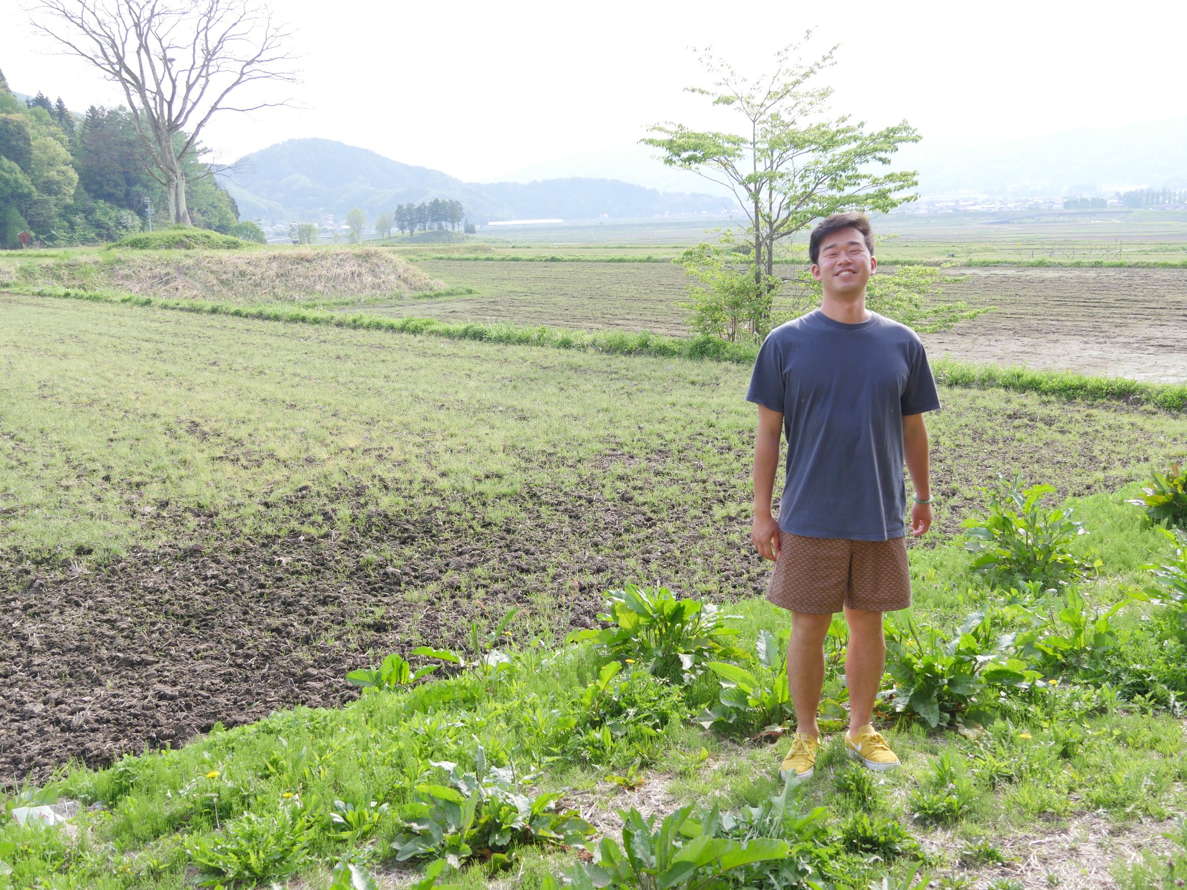 田んぼのあぜ道でこちらを見てほほ笑む原田峻佑さん