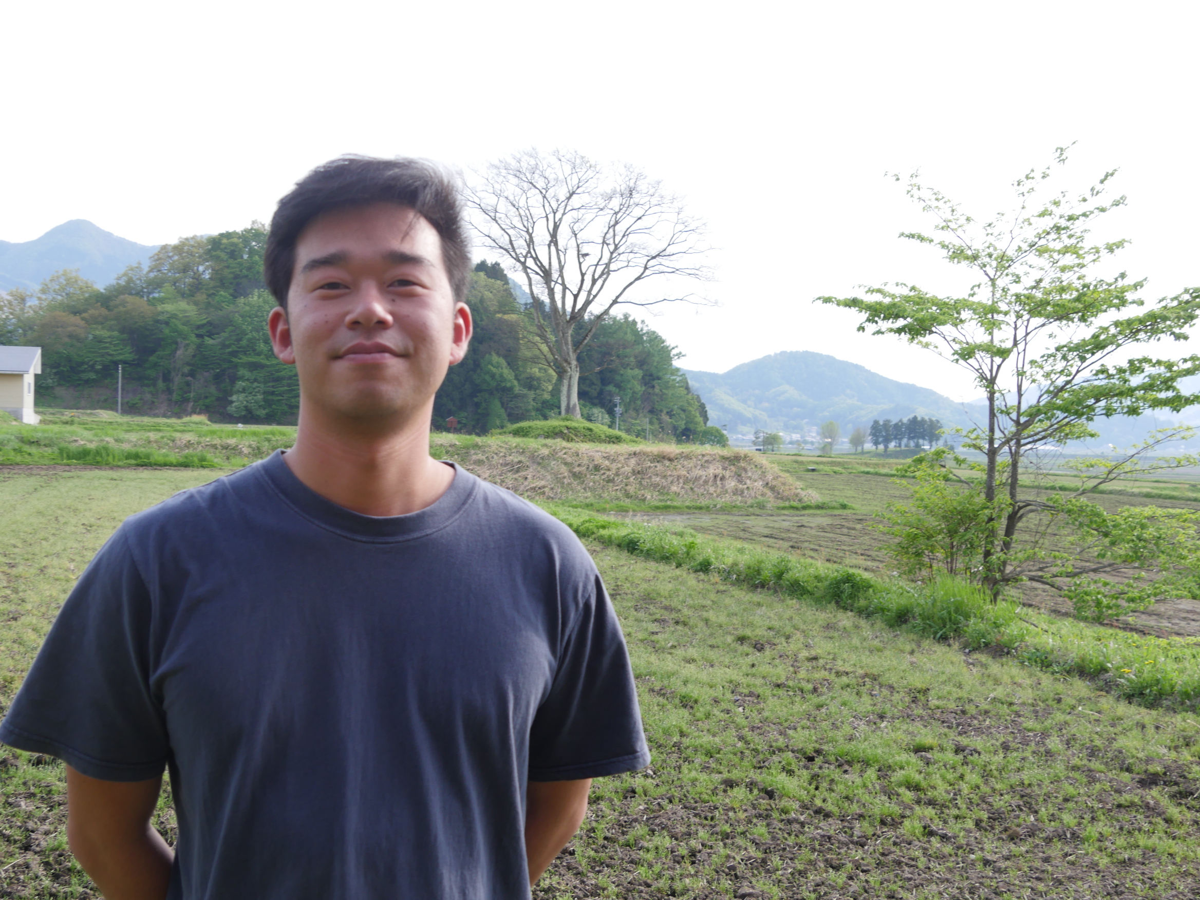 木島平村の景色をバックにカメラに向かってほほ笑む原田峻佑さん